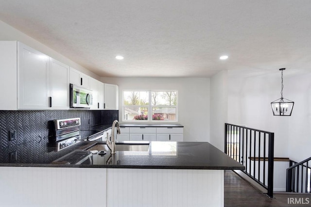kitchen featuring a sink, a peninsula, stainless steel appliances, tasteful backsplash, and white cabinetry