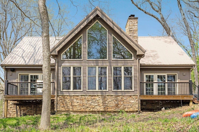 back of property with stone siding, a deck, and a chimney