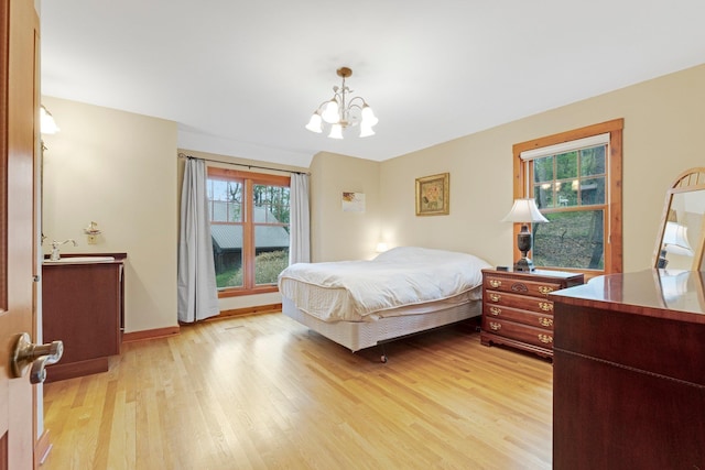 bedroom with baseboards, a notable chandelier, and light wood-style floors