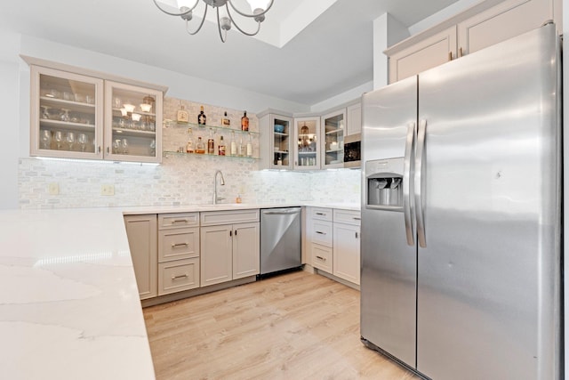 kitchen featuring light wood finished floors, a sink, stainless steel appliances, a notable chandelier, and backsplash