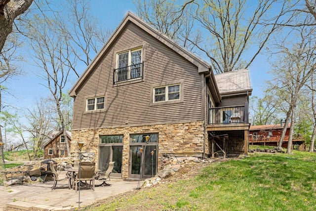 rear view of property with a deck, a patio, stone siding, and a lawn