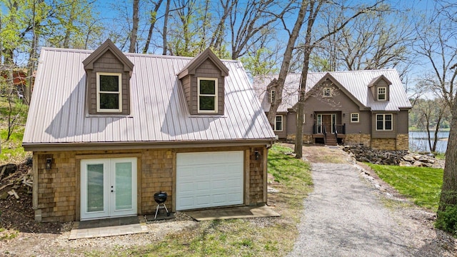 cape cod home featuring an attached garage, driveway, french doors, and metal roof