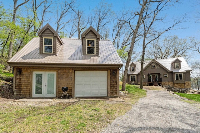 new england style home featuring a garage, driveway, french doors, and metal roof