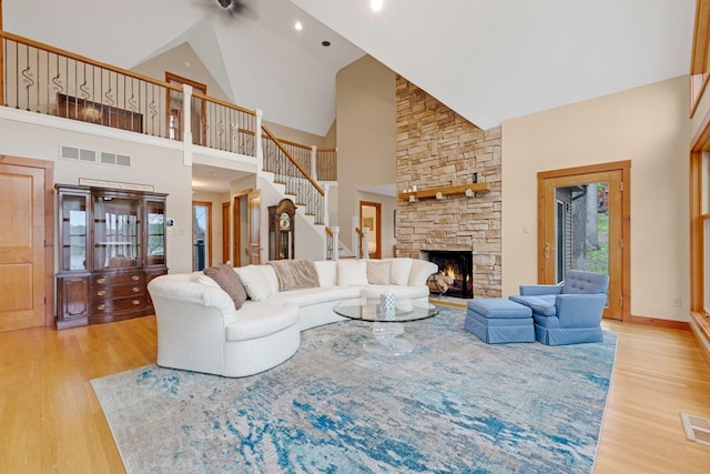 living area with light wood-style flooring, a stone fireplace, ceiling fan, stairs, and high vaulted ceiling