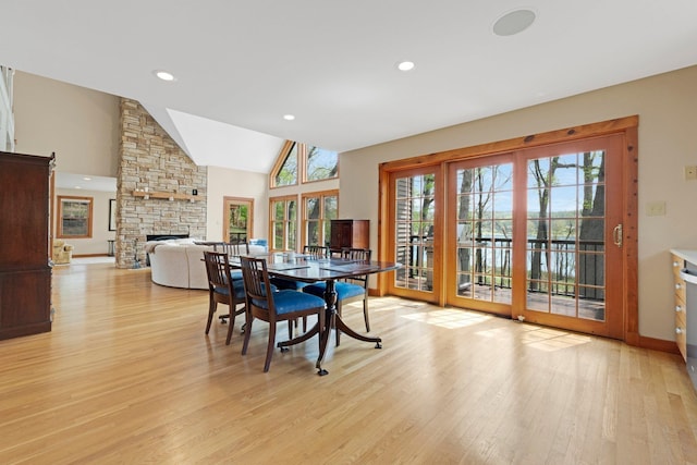 dining space featuring a fireplace, light wood finished floors, lofted ceiling, and a healthy amount of sunlight