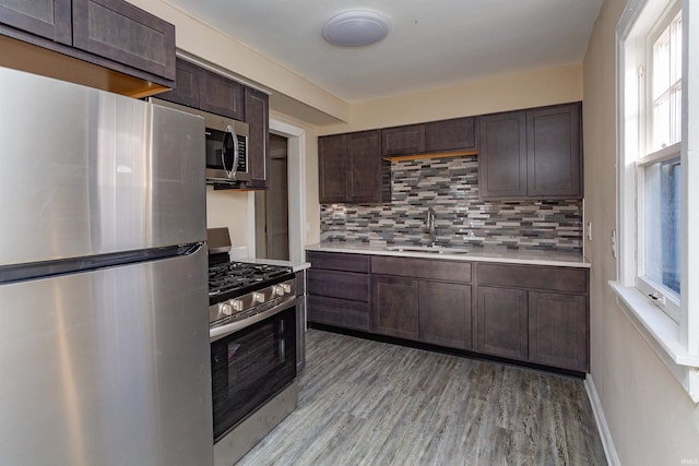 kitchen with a sink, decorative backsplash, light countertops, dark brown cabinets, and appliances with stainless steel finishes