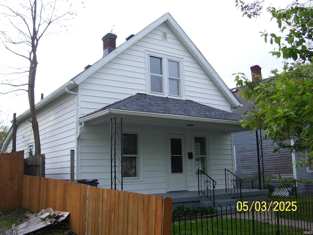 bungalow featuring a shingled roof, a porch, a chimney, and a fenced front yard
