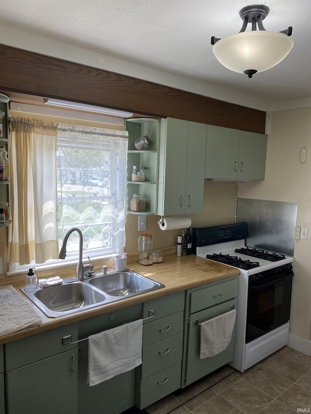 kitchen with a sink, open shelves, green cabinets, light countertops, and gas stove