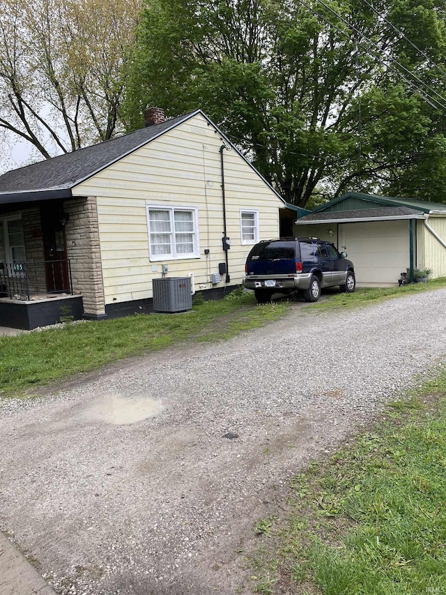 view of side of home with an outdoor structure, stone siding, a chimney, gravel driveway, and central AC unit