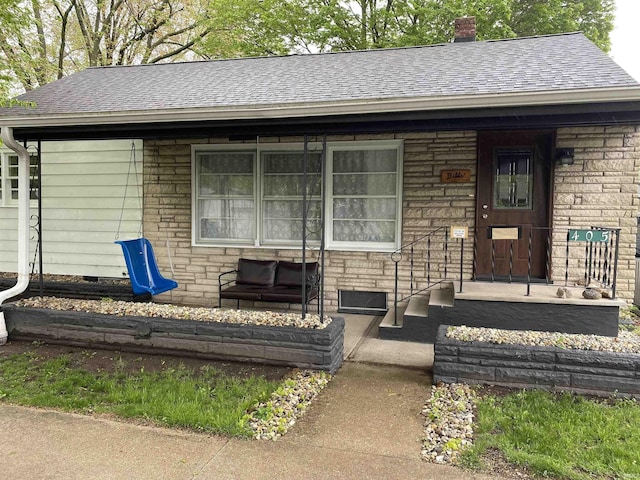property entrance with stone siding, a shingled roof, and a chimney