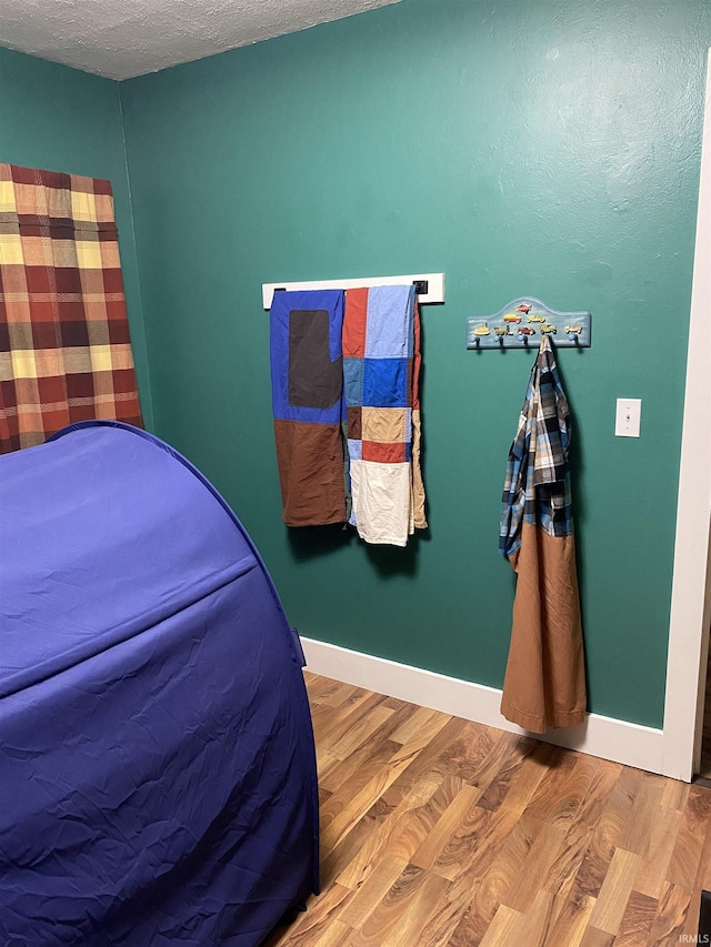 bedroom with a textured ceiling, wood finished floors, and baseboards