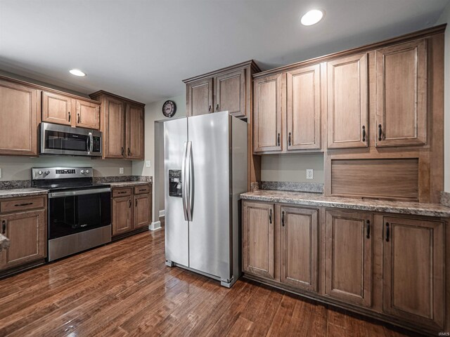 kitchen featuring recessed lighting, stainless steel appliances, light stone counters, and dark wood-style floors