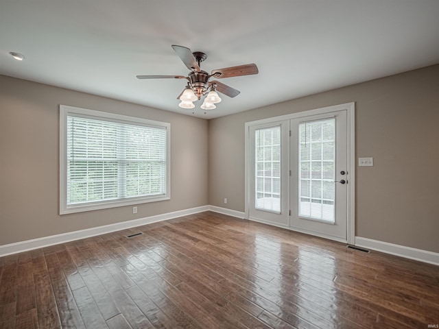 empty room featuring a ceiling fan, dark wood-style flooring, baseboards, and visible vents