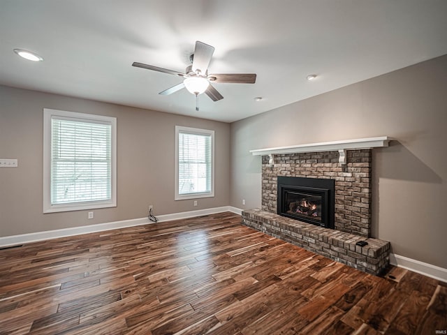 unfurnished living room with ceiling fan, wood finished floors, baseboards, and a brick fireplace