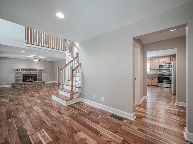 unfurnished living room with wood finished floors, stairway, visible vents, ceiling fan, and a stone fireplace