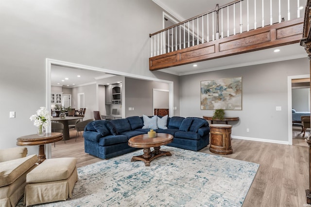 living area featuring ornamental molding, light wood-style flooring, baseboards, and a high ceiling