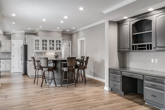 kitchen featuring a breakfast bar, freestanding refrigerator, tasteful backsplash, ornamental molding, and recessed lighting