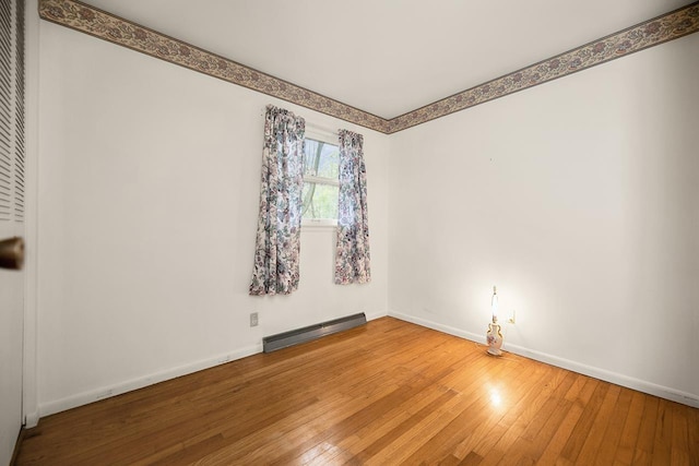 empty room with wood-type flooring, baseboards, and a baseboard heating unit