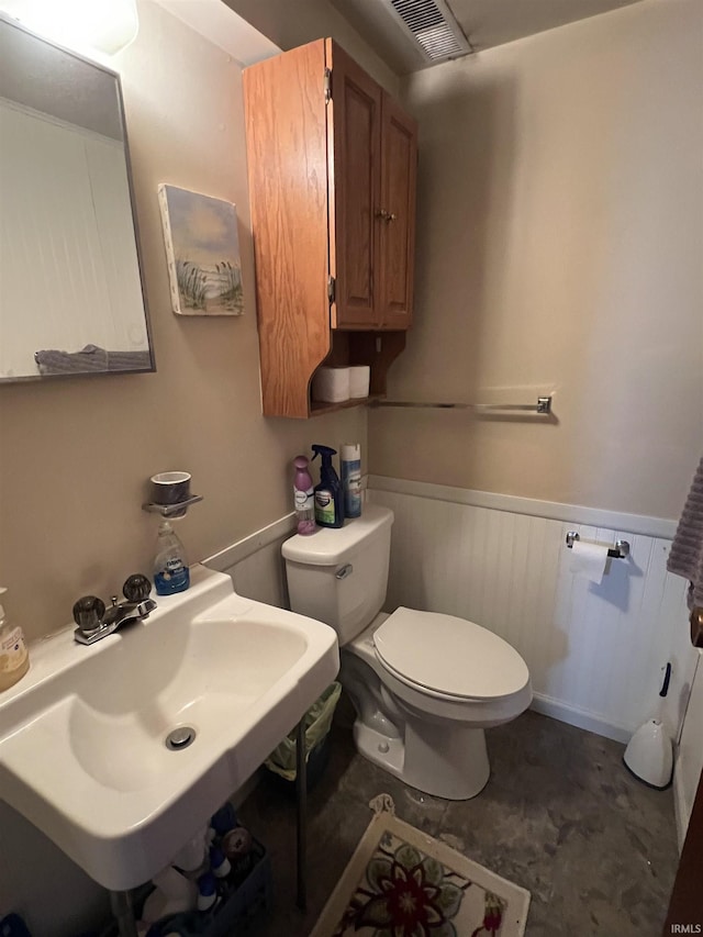 half bathroom featuring toilet, a sink, visible vents, and a wainscoted wall
