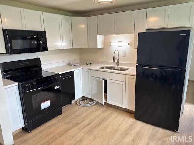 kitchen with light wood-style flooring, a sink, white cabinetry, black appliances, and light countertops