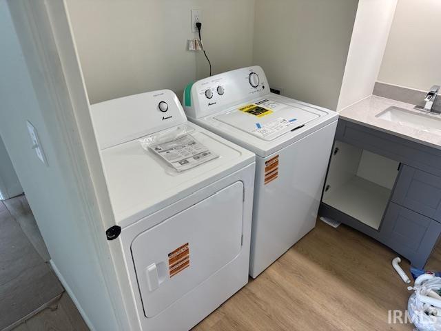 washroom with washing machine and dryer, laundry area, a sink, and light wood-style floors