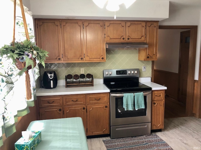 kitchen with under cabinet range hood, backsplash, light countertops, and electric range