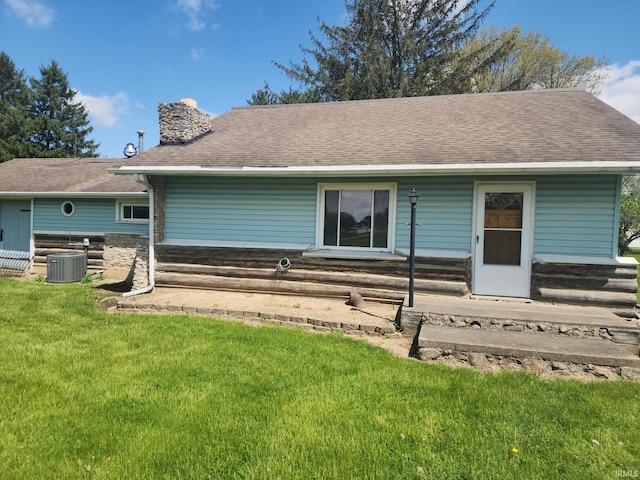 back of property featuring a shingled roof, a chimney, and a lawn