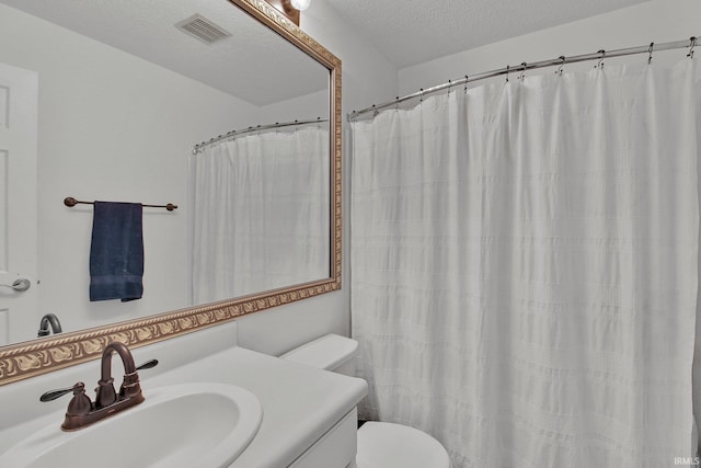 full bath featuring toilet, vanity, visible vents, and a textured ceiling