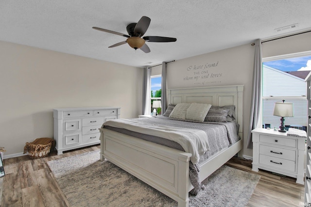 bedroom with a textured ceiling, baseboards, light wood-type flooring, and a ceiling fan