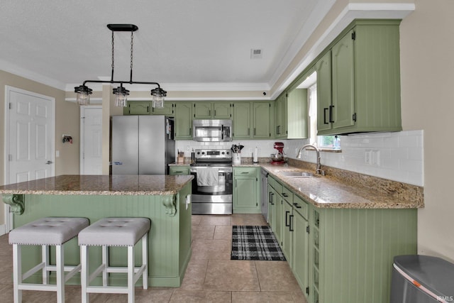 kitchen featuring a kitchen bar, a sink, green cabinetry, stainless steel appliances, and ornamental molding