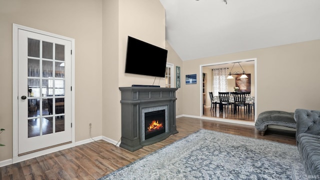 living area featuring vaulted ceiling, a lit fireplace, baseboards, and wood finished floors