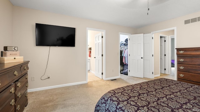 bedroom with ensuite bathroom, light colored carpet, visible vents, a walk in closet, and baseboards