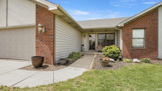 view of exterior entry with a lawn, brick siding, and a garage