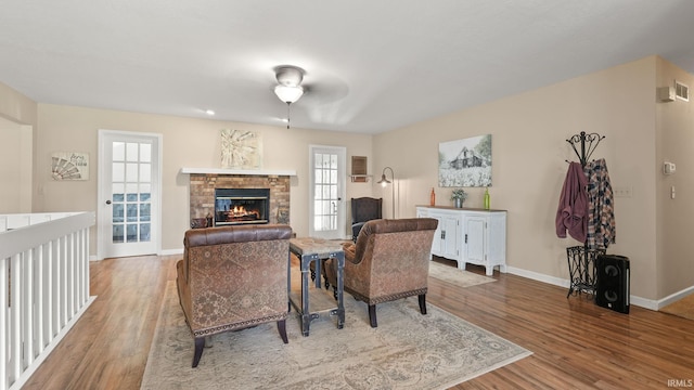 living room featuring baseboards, a stone fireplace, ceiling fan, and wood finished floors
