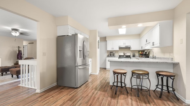 kitchen featuring under cabinet range hood, a peninsula, light wood finished floors, and appliances with stainless steel finishes