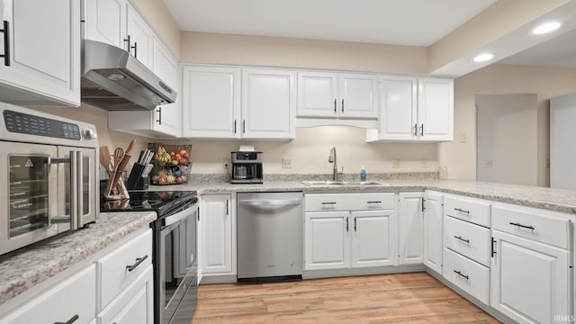 kitchen with white cabinetry, under cabinet range hood, appliances with stainless steel finishes, and a sink
