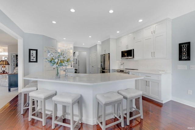 kitchen with wood finished floors, backsplash, a kitchen bar, white cabinets, and appliances with stainless steel finishes