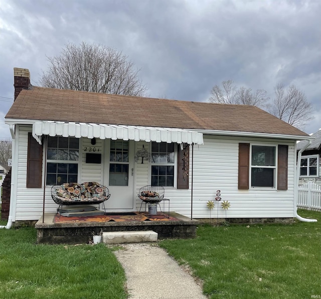 view of front of house featuring a chimney, a front yard, and roof with shingles