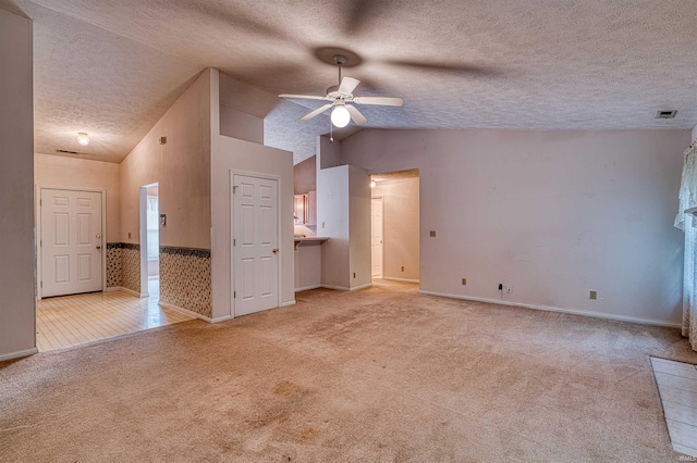 unfurnished living room featuring vaulted ceiling, light colored carpet, a textured ceiling, and a ceiling fan