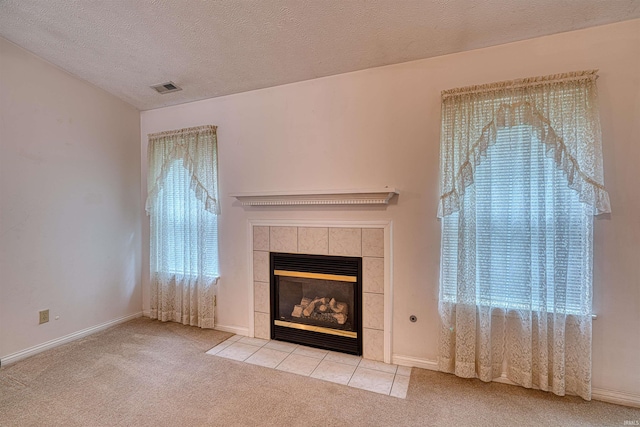 unfurnished living room featuring a textured ceiling, carpet, visible vents, baseboards, and a tiled fireplace