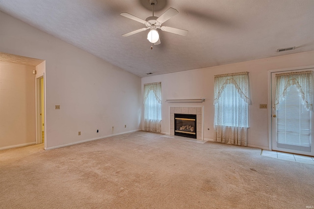 unfurnished living room with lofted ceiling, a ceiling fan, a tile fireplace, visible vents, and light carpet