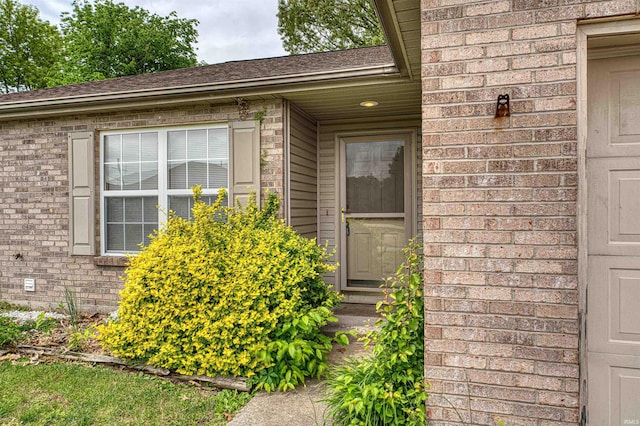 entrance to property featuring brick siding and roof with shingles