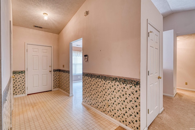 entryway with vaulted ceiling, a wainscoted wall, a textured ceiling, and visible vents