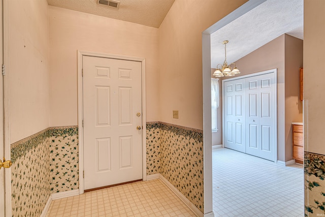 foyer entrance featuring a textured ceiling, baseboards, an inviting chandelier, visible vents, and wainscoting