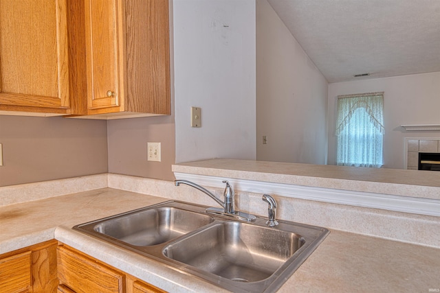 kitchen featuring a sink, a fireplace, visible vents, light countertops, and vaulted ceiling