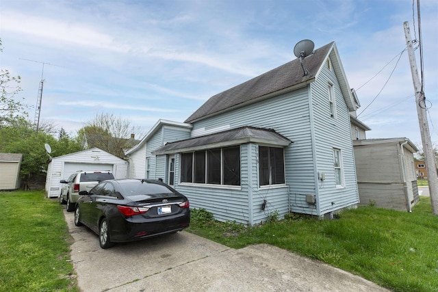 view of side of home featuring a sunroom, a shingled roof, an outdoor structure, a yard, and a detached garage