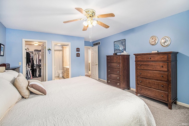 bedroom with a closet, visible vents, light carpet, a walk in closet, and baseboards