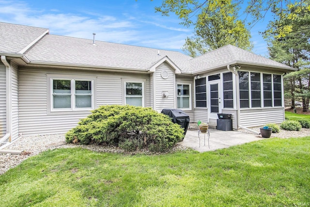 back of house with a yard, roof with shingles, a sunroom, and a patio