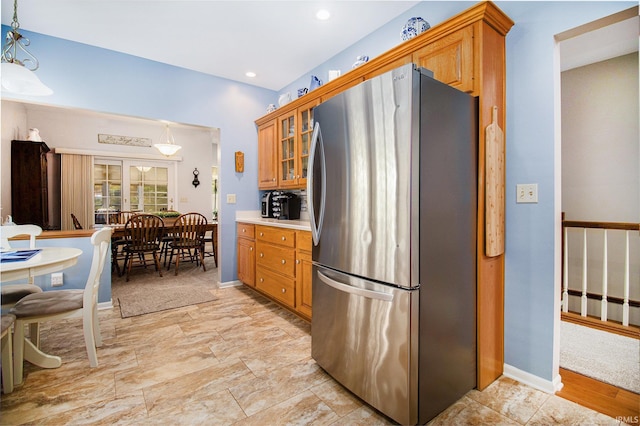kitchen featuring freestanding refrigerator, pendant lighting, glass insert cabinets, brown cabinetry, and light countertops