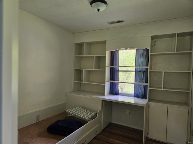 unfurnished office featuring built in desk, visible vents, and dark wood-style floors